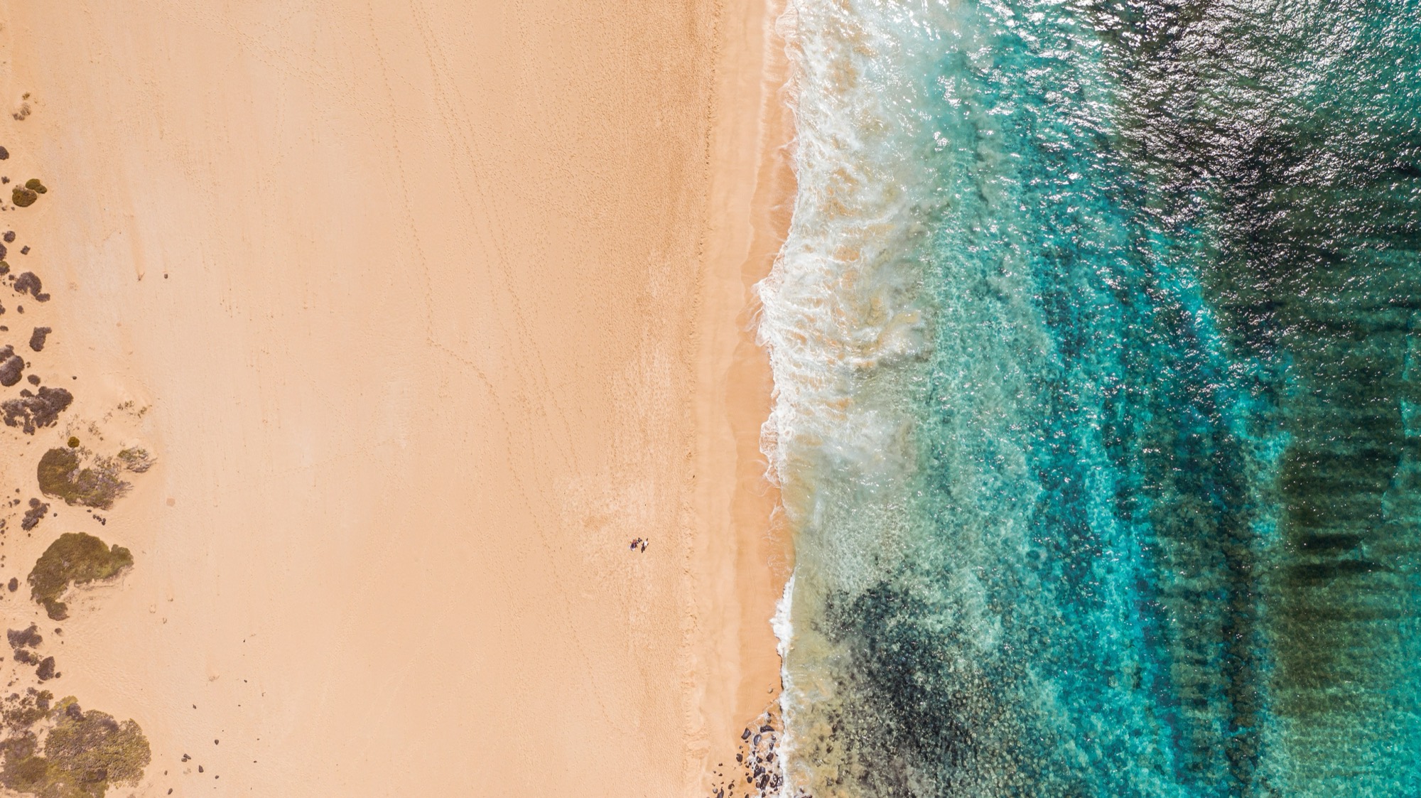 Vista cenital de una playa de Lanzarote con la espuma rompiendo sobre la arena dorada