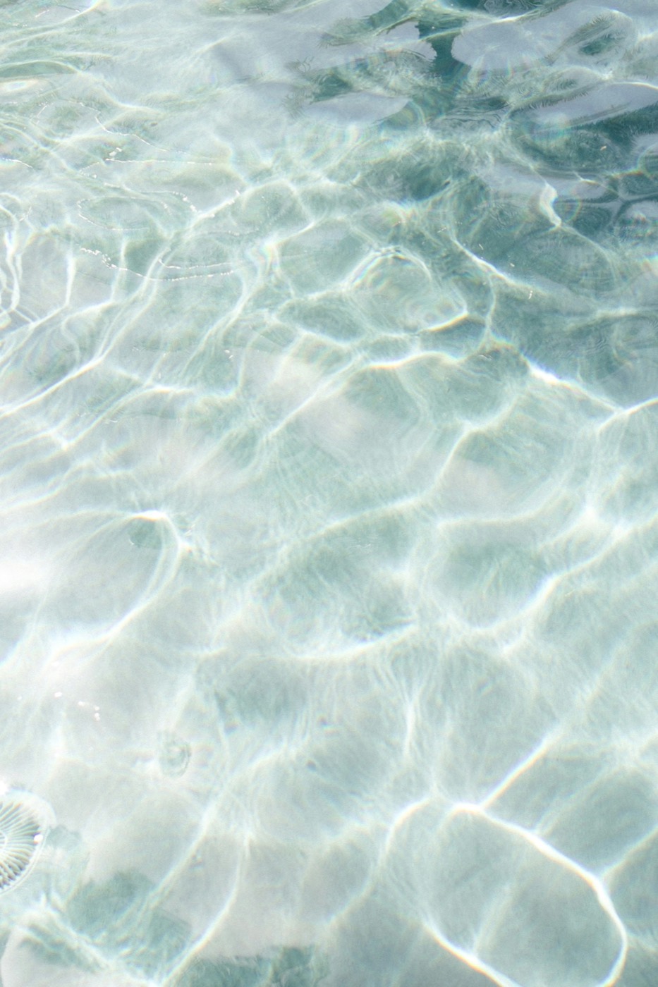 Agua transparente con las ondas de luz dibujadas sobre el fondo de arena